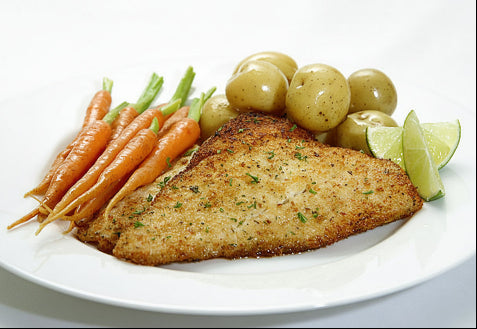 Plated dish with breaded fish, carrots, green beans, and olives on a white plate.